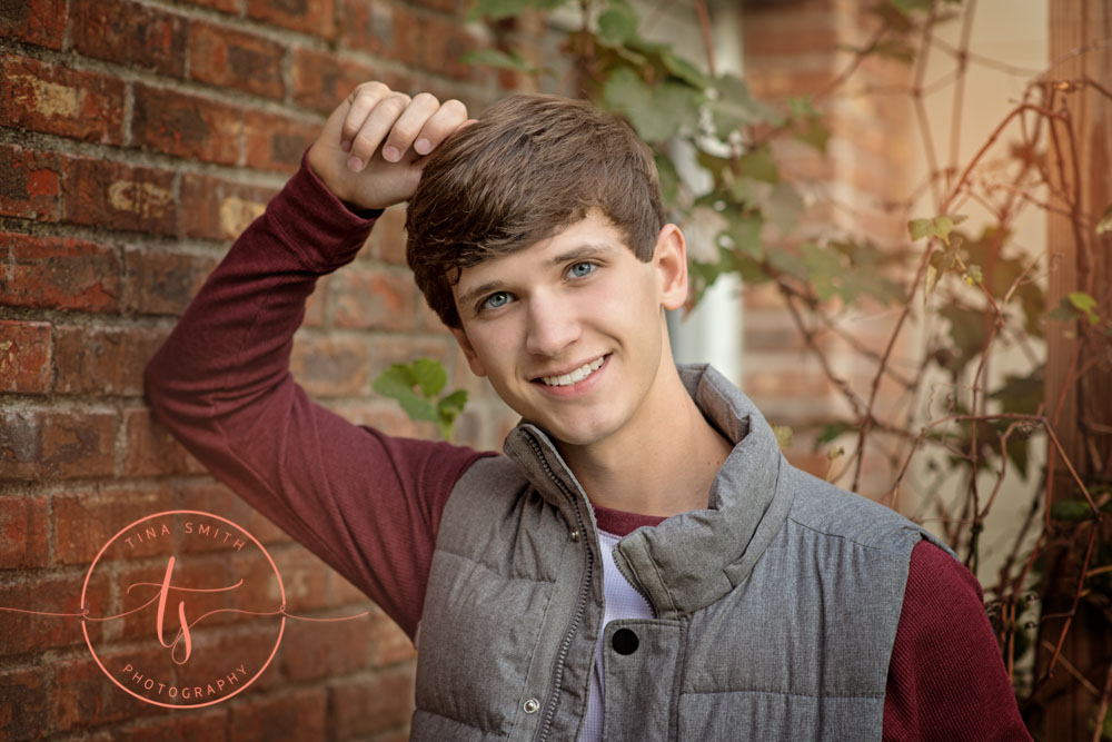 young male high school senior leaning against brick wall wearing vest