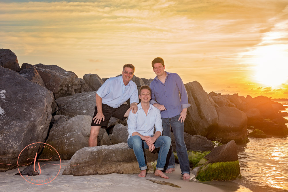 family sitting on rocks at destin jetties at sunset