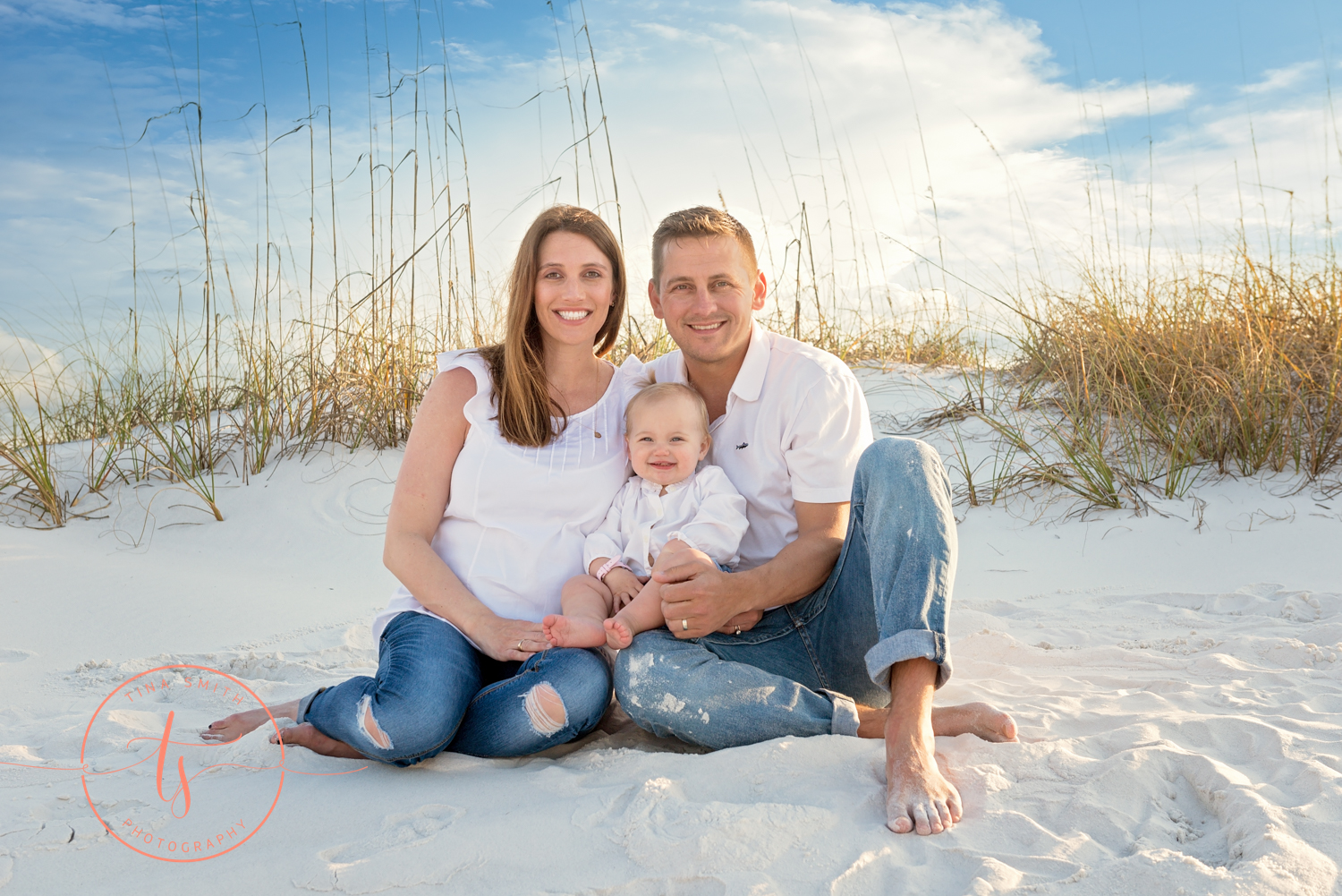 mom dad baby sitting on beach in destin smiling for photographer