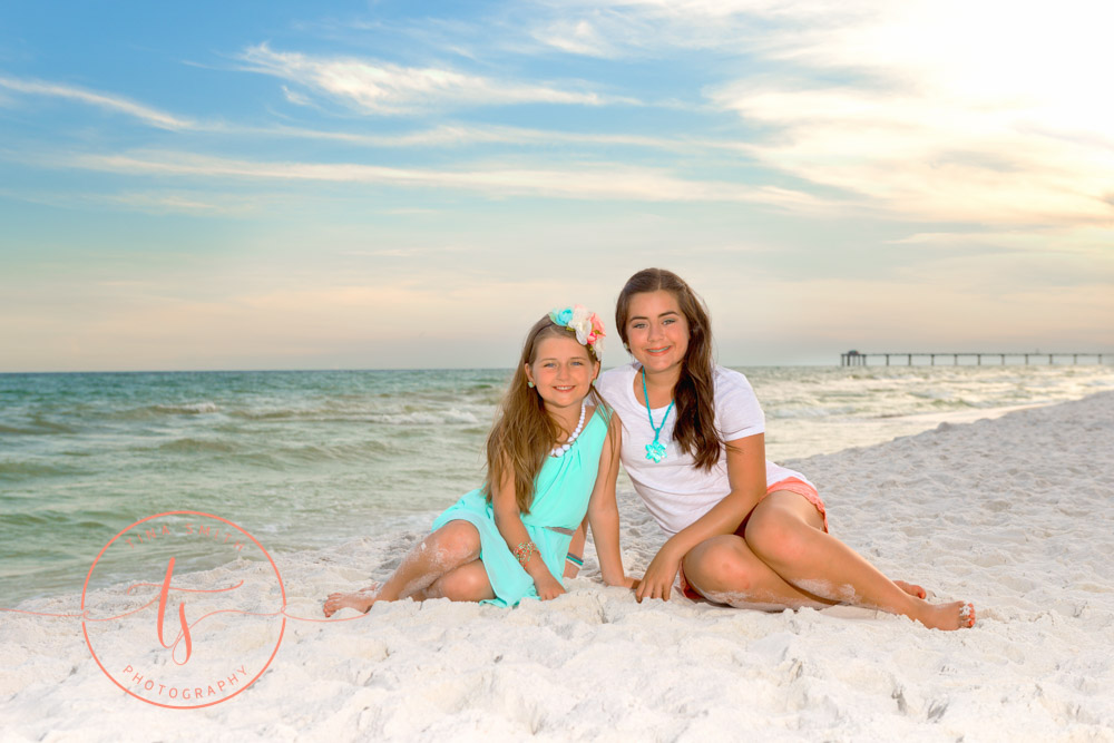 sisters sitting on destin beach posing for photographer