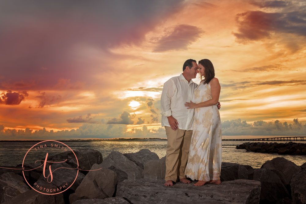 couple standing on rock in ocean at sunset