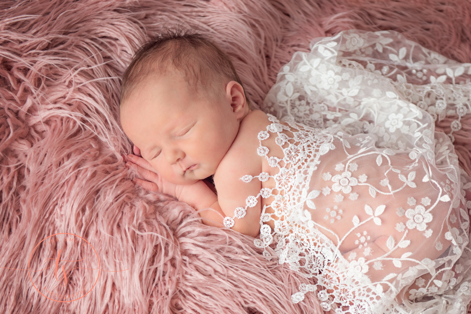 newborn baby on pink fur wrapped in white lace