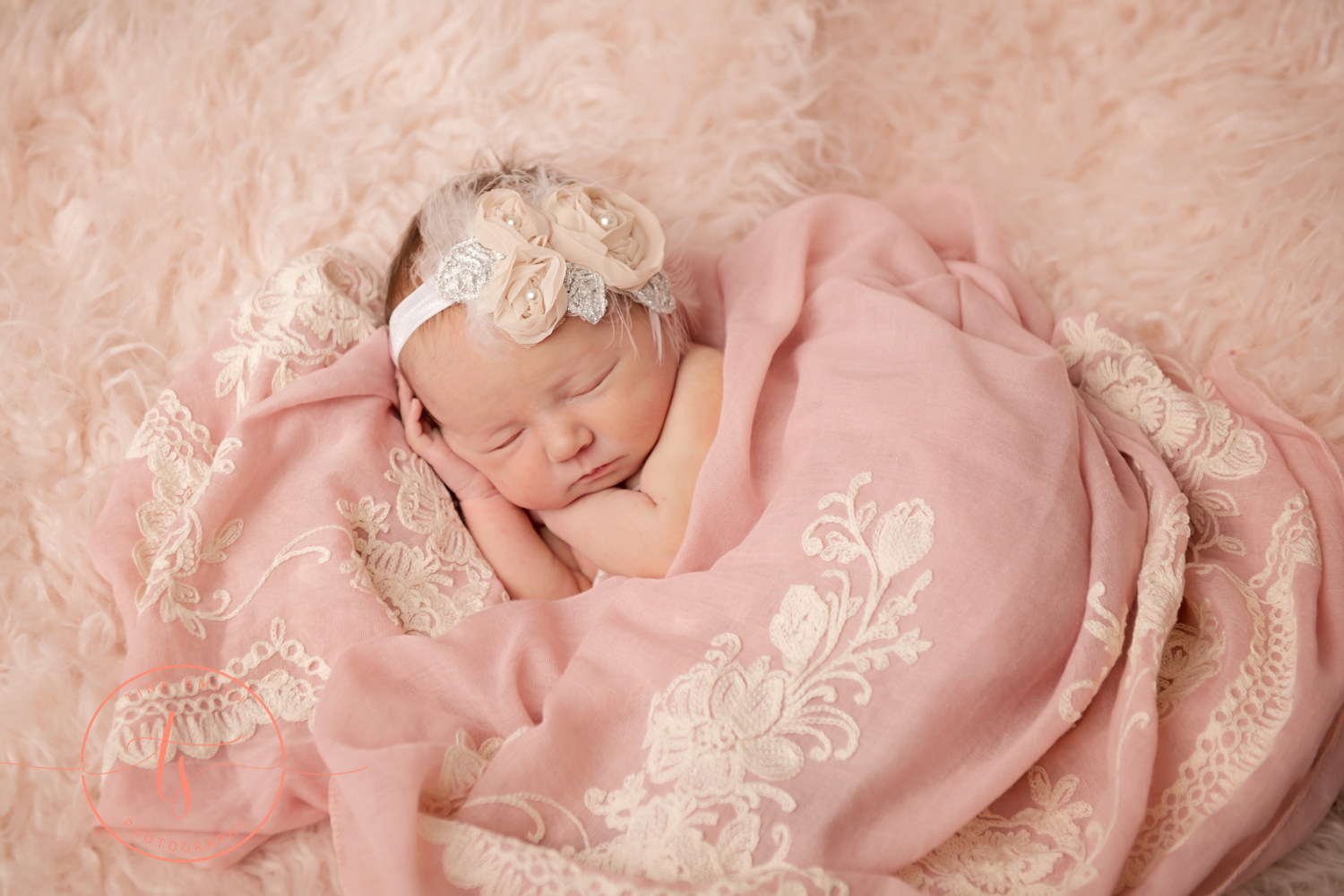 newborn baby on beige fur with pink flowered wrap posed for pictures