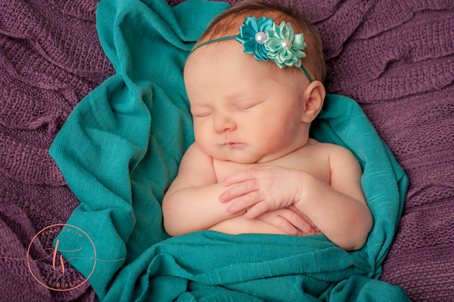 newborn baby wrapped in teal on purple blanket