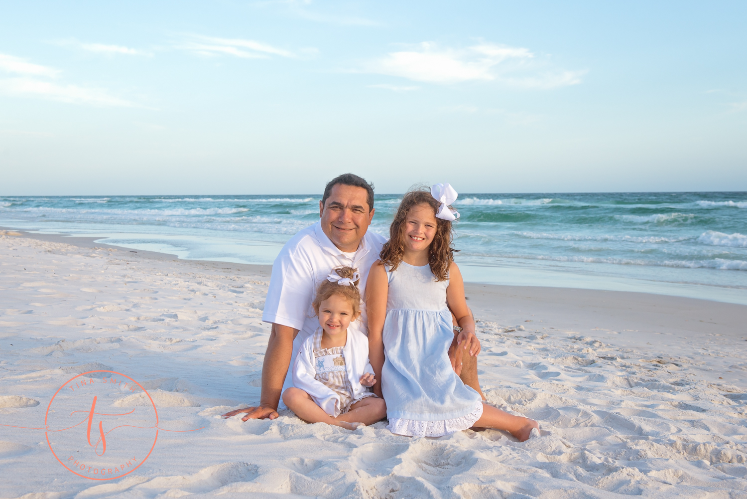 dad and daughters sitting on watersound beach smiling for photographer