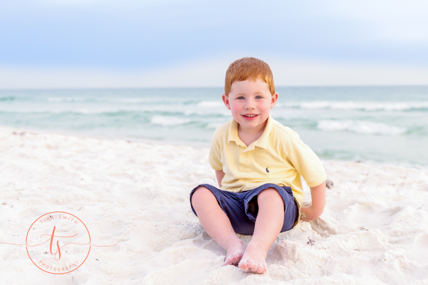 red headed little boy sitting on the beach in destin playing in the sand