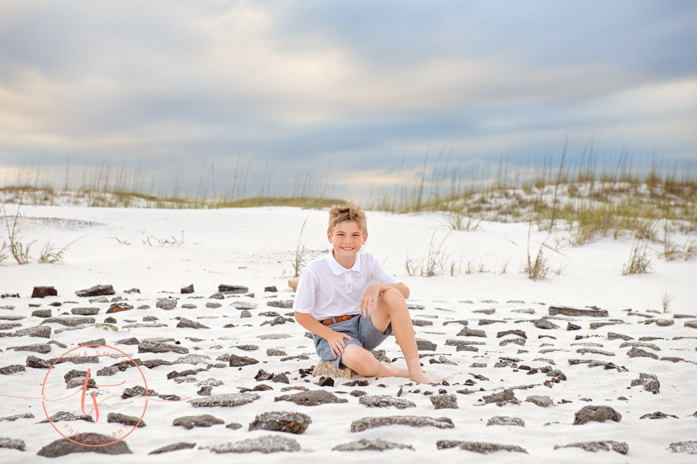 boy sitting in ring of rocks on beach