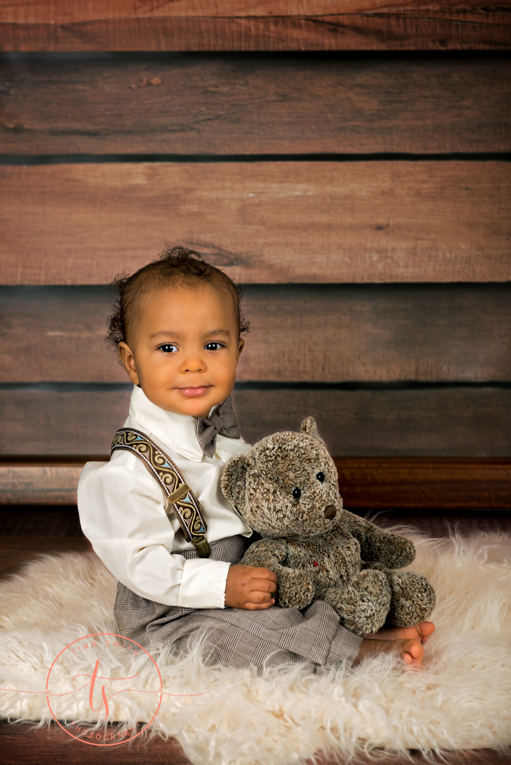 boy holding bear sitting on rug smiling for photographer