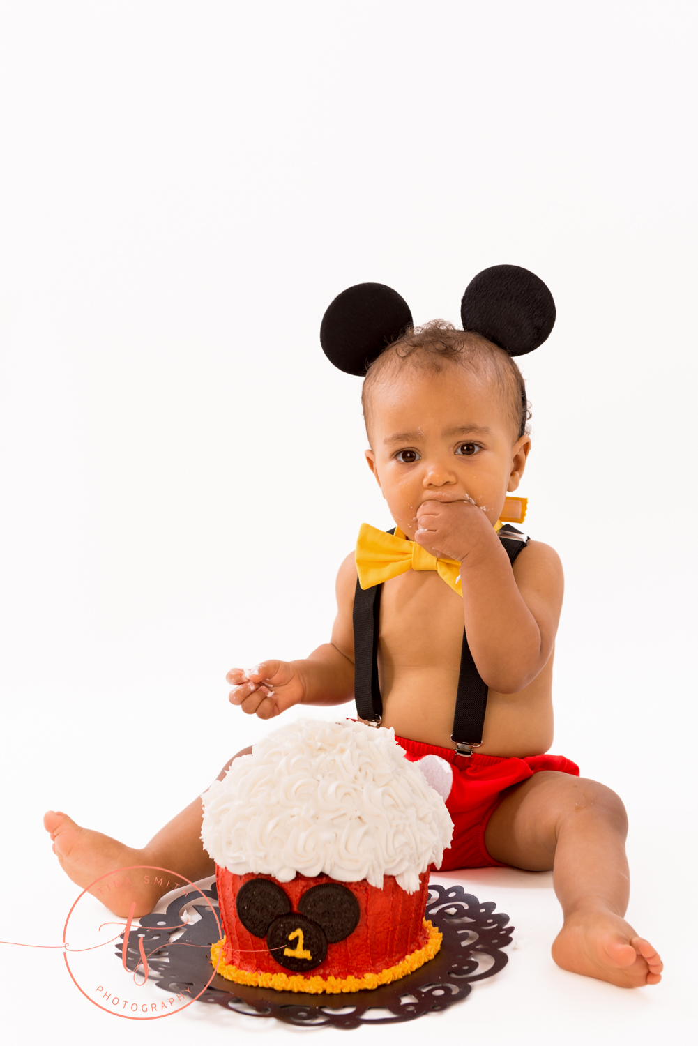 boy wearing mickey mouse ears eating cake for 1 year cake smash