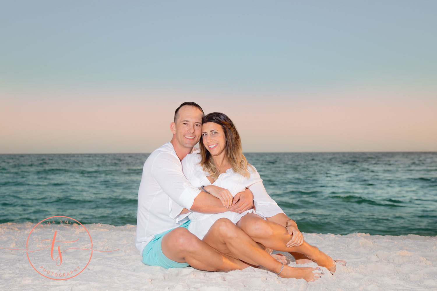 couple sitting on beach smiling for photography 