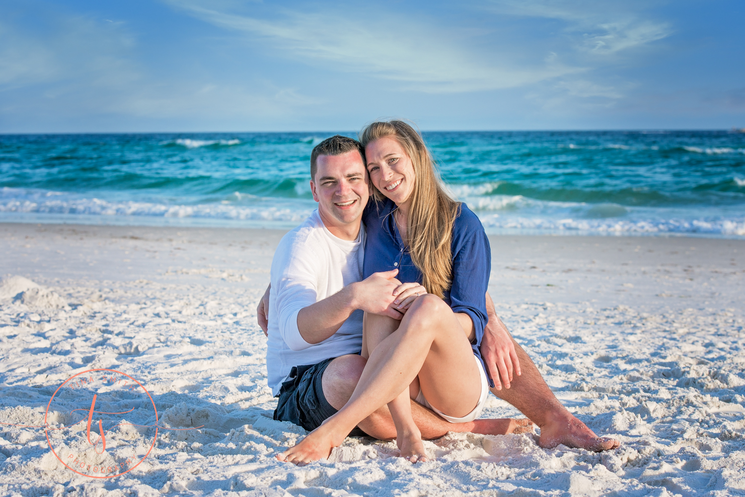 couple sitting on beach huggins showing off engagement ring