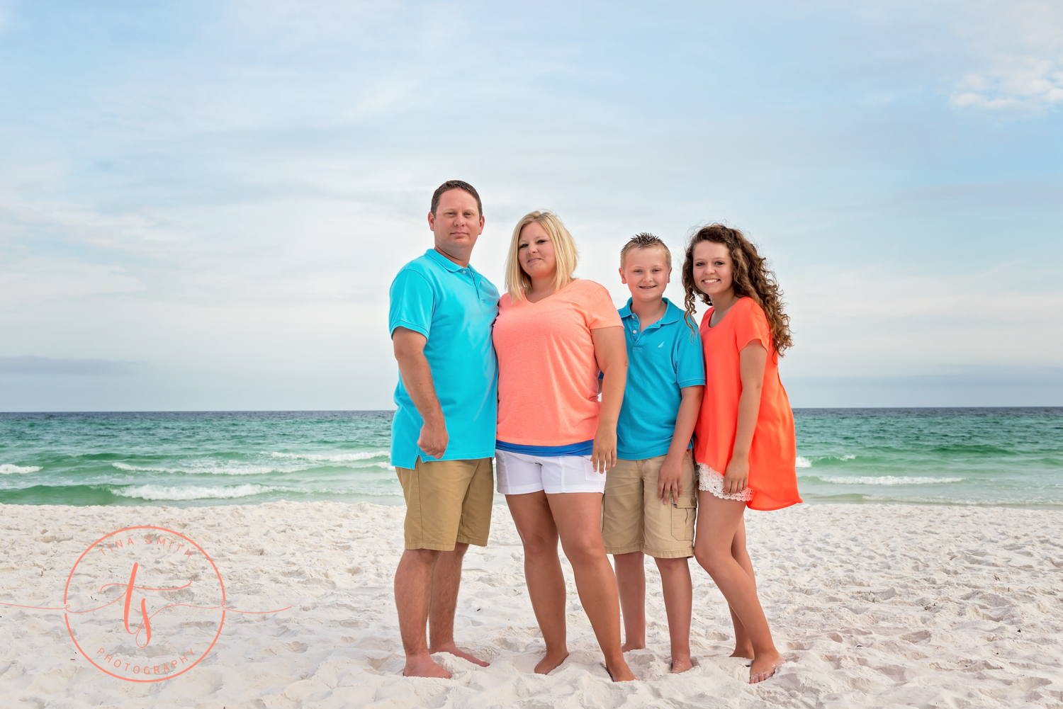 family wearing teal and orange standing on beach for portraits