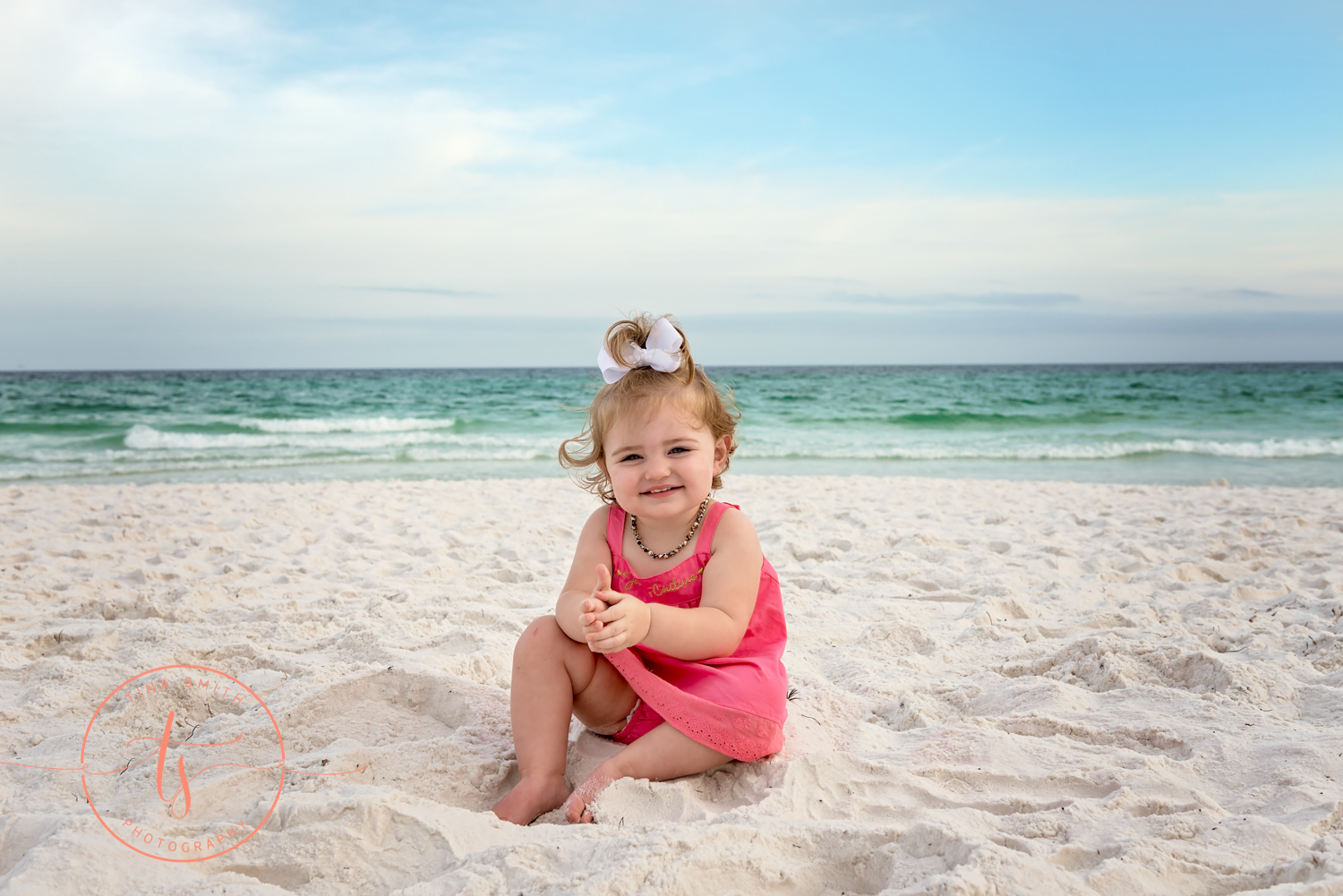 baby girl sitting in beach sand smiling for camera