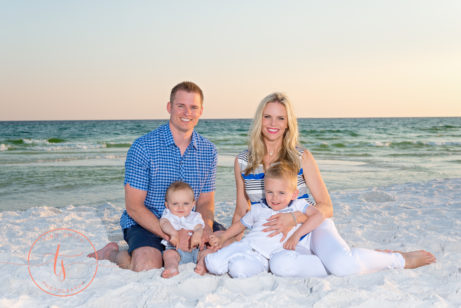 mom dad and 2 sons sitting on beach in destin at sunset