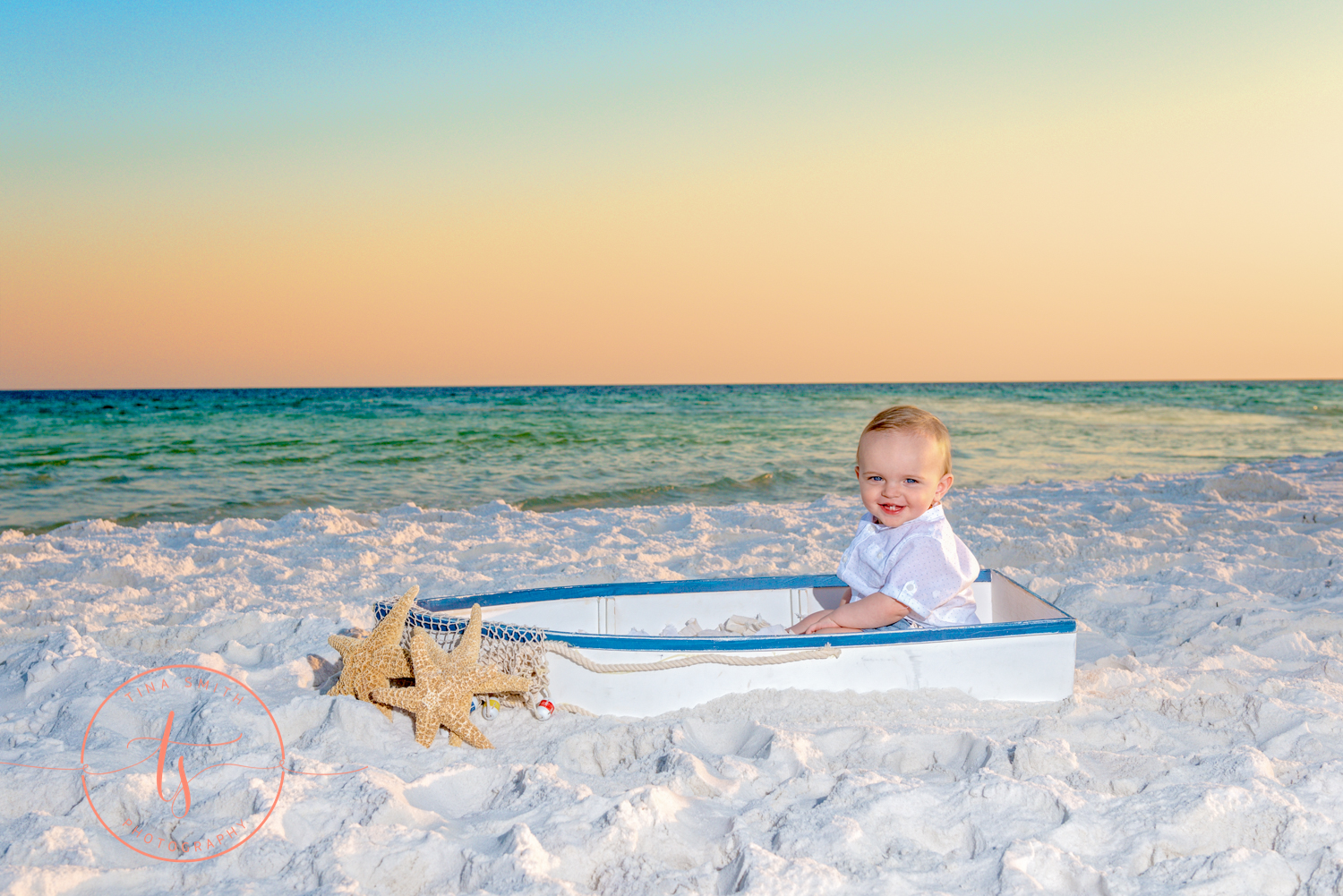 1 year boy sitting in a boat on beach smiling for photography