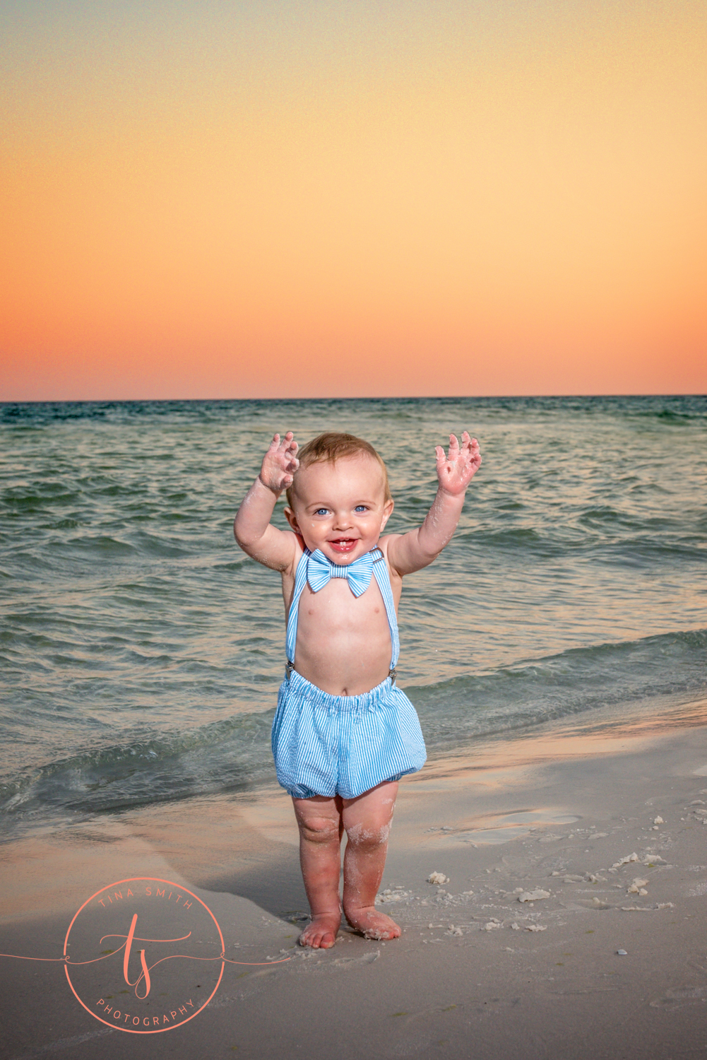 little boy in birthday romper playing on the beach at sunset