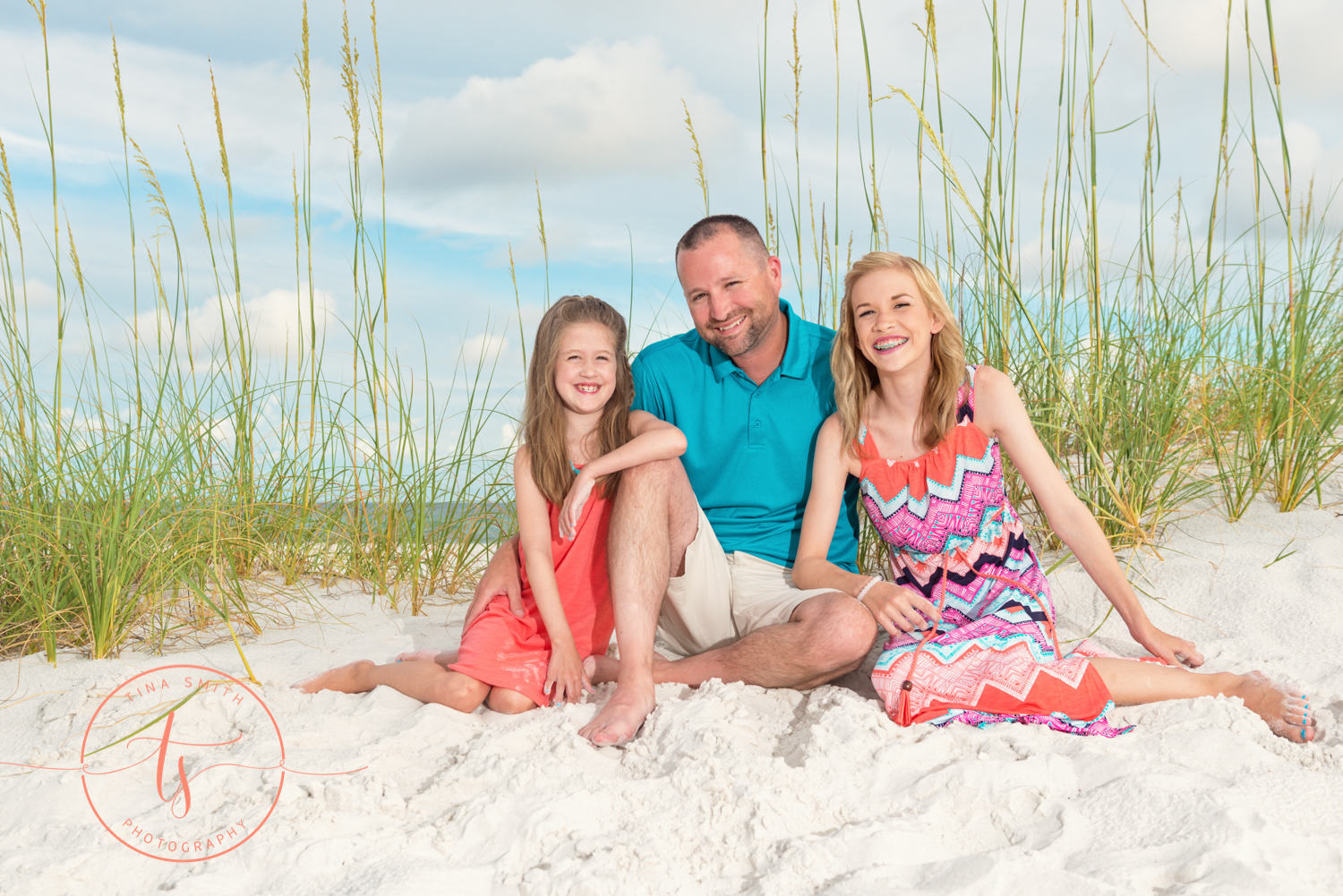 dad and daughters sitting on the beach smiling for destin photography