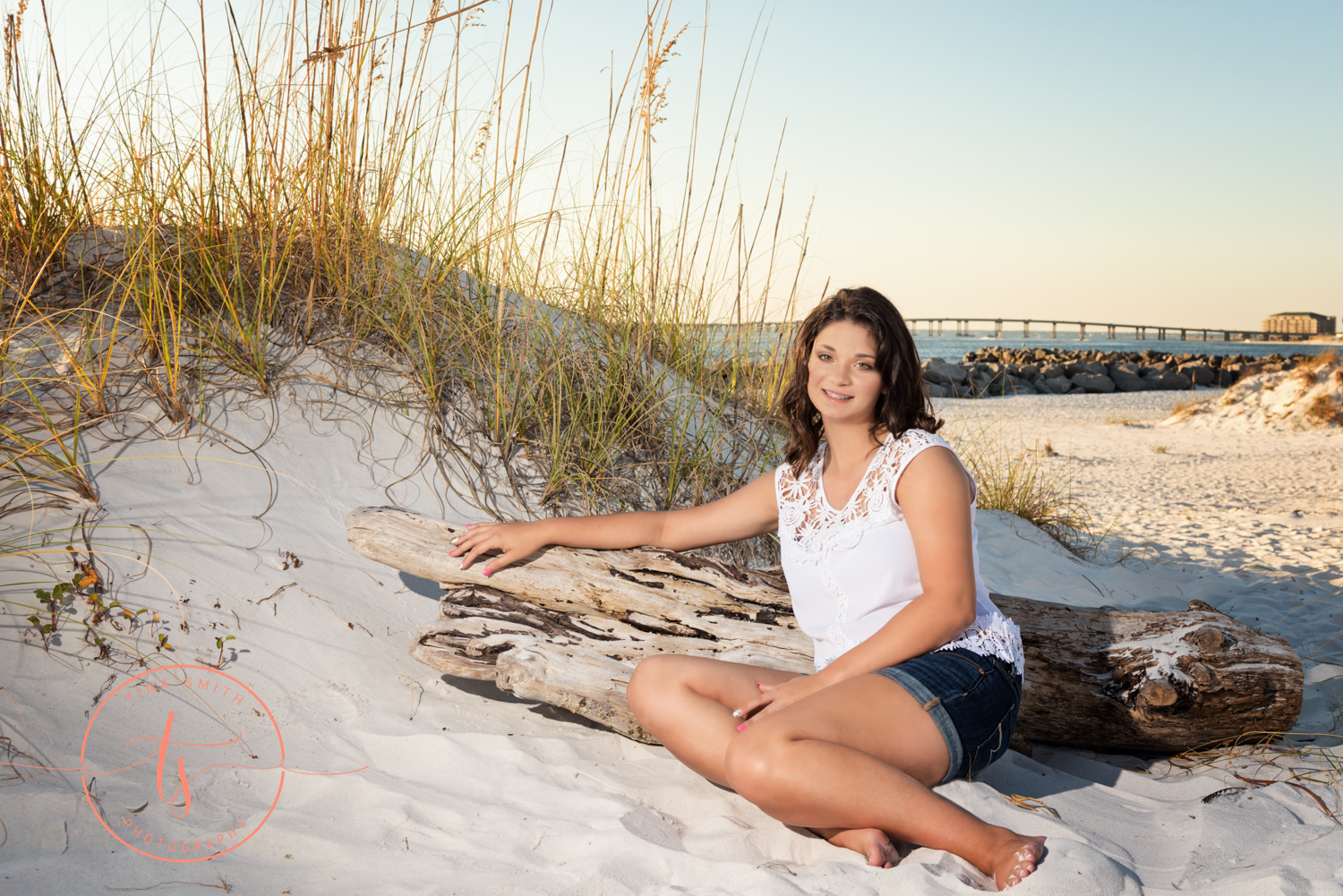 senior girl dressed in white leaning on driftwood on the beach in destin