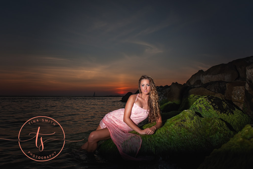 girl in pink dress lying in the water at sunset for destin senior portraits