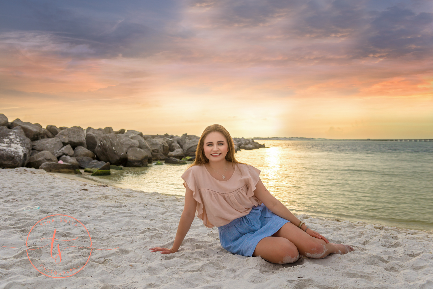senior girl sitting on the beach at sunset smiling