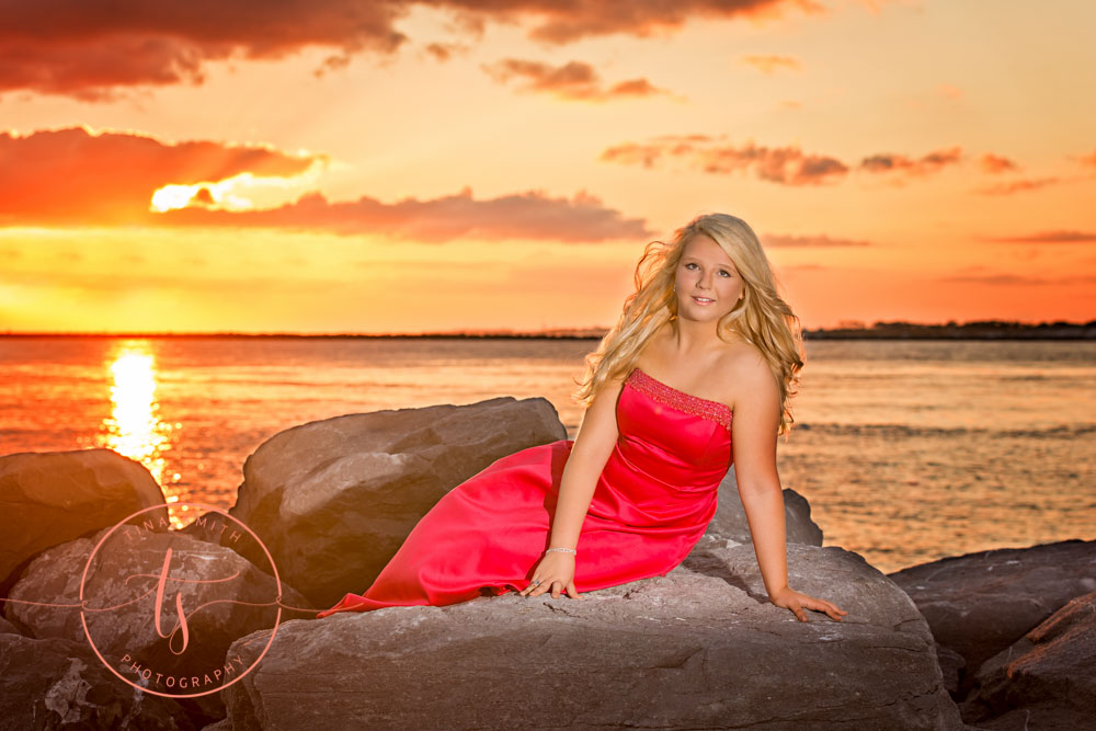 girl in pink formal gown laying on rocks at sunset on the beach for destin senior portrait photographer