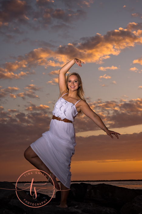 senior girl doing a dance pose on rock on destin beach