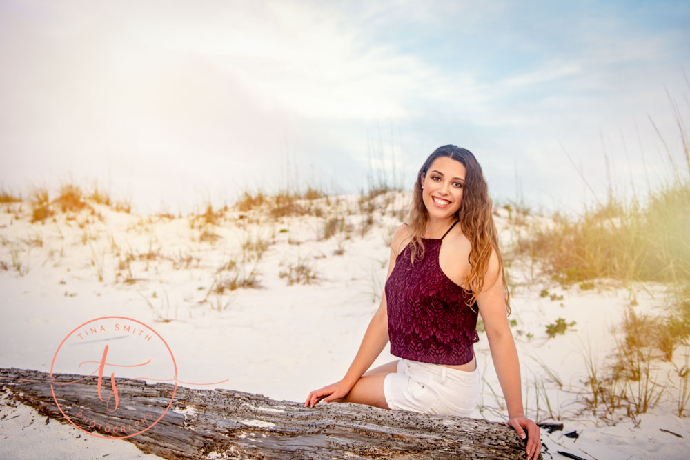 senior girl sitting on a log on beach in destin