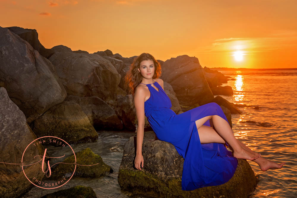 senior girl in blue dress posing on rock in water in destin