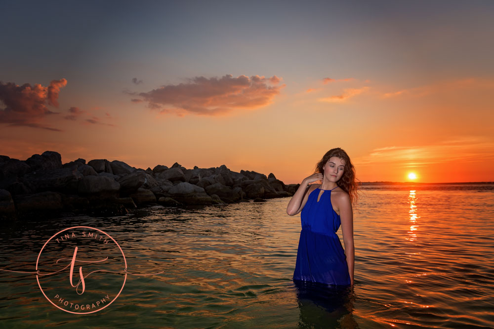 senior girl in blue dress posing in water at sunset in destin