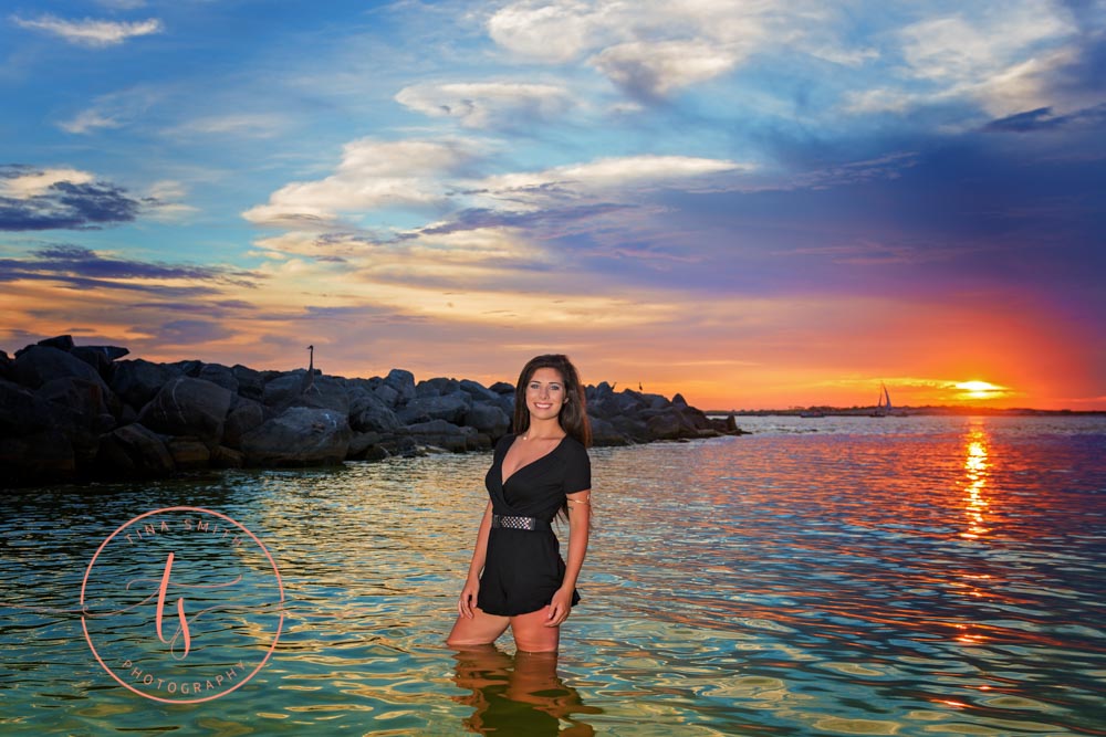 senior girl in black romper posing in water in destin