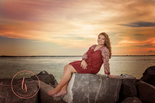 senior girl sitting on jetty in destin at sunset