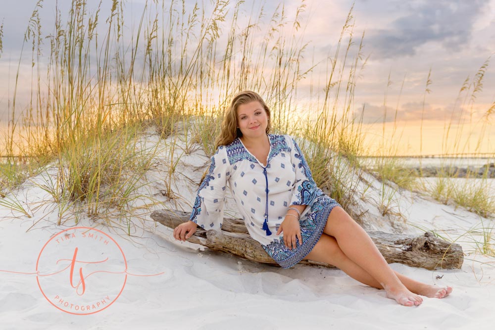 senior girl sitting on drift wood on beach in destin